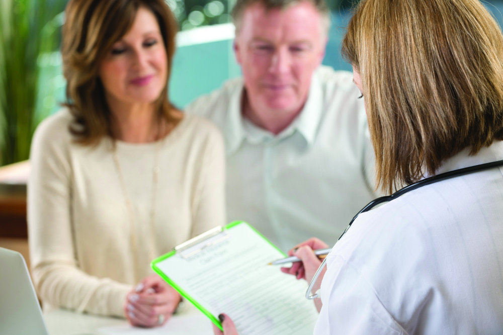 Doctor filling out insurance form with mature couple. Shallow focus